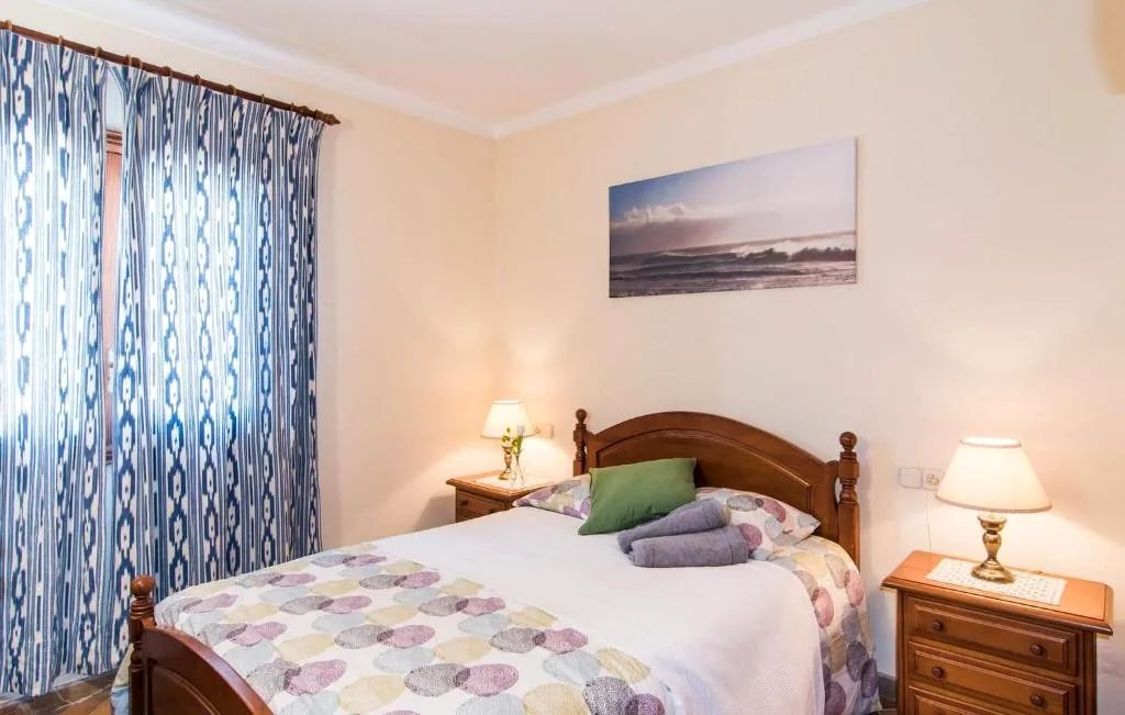 Double bedroom with wooden bed, blue patterned curtains, and bedside lamps
