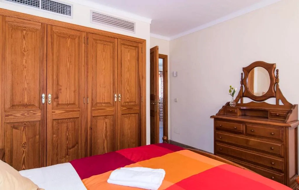 Double bedroom with red and orange bedding, wooden wardrobe, and dresser